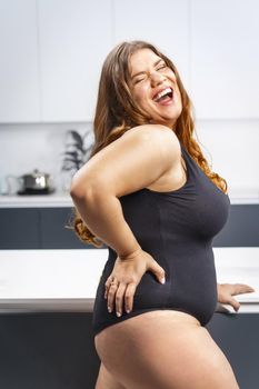 Young fat woman trying diet. Girl standing next to the kitchen table. Diet young fat woman standing on kitchen. Close up chubby female lowering BMI weight. Trying to loose weight fast. 