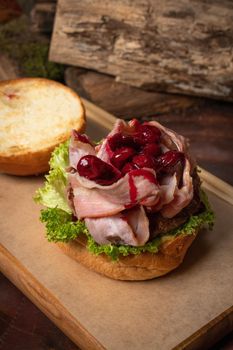 Creative craft burger disassembled with fried slices of bacon and cherry sweet and sour sauce on top, fresh lettuce with lead bun laying next to it. Restaurant concept. Street food concept. 