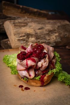 Disassembled creative craft burger with fried slices of bacon and cherry sweet and sour sauce on top, fresh lettuce with lead bun laying next to it. Restaurant concept. Street food concept. 