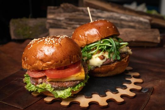 Two amazing fresh beef burgers served with french fries, one with fried walnuts and grilled cheese on a decorative wooden part of simple mechanism. Restaurant concept. Fast food, street food concept. 