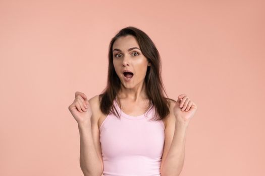 Acting young woman expressing OMG wearing pink t-shirt with hands on her face, excited and joy expression on her face with positive emotions. Facial expressions, emotions, feelings.