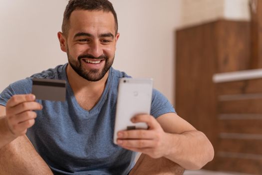 Using smartphone handsome bearded guy holding debit or credit card in hands buying online. Modern digital life. Digital app on smartphone. 