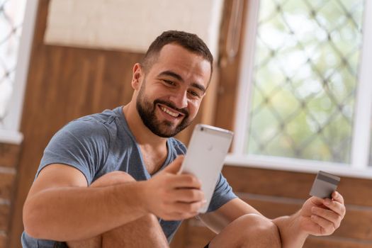 Happy handsome bearded guy with smartphone and debit or credit card in hands buying online. Modern digital life. Digital app on smartphone. 