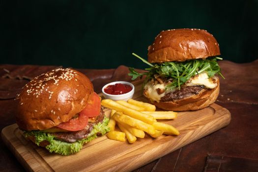 Fresh American amazing beef burgers served with French fries, one with fried walnuts, grilled cheese on decorative wooden part of simple mechanism. Restaurant concept. Fast food, street food concept. 