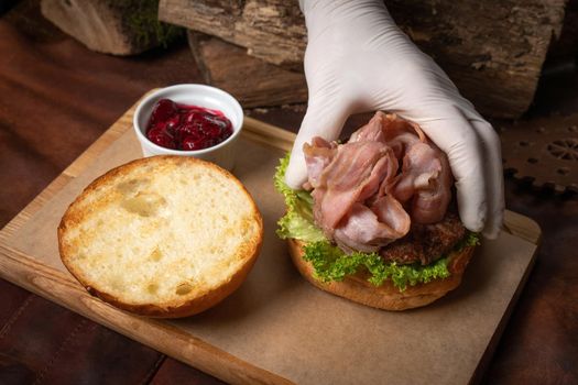 Craft fresh burger with fresh slices of bacon served with sweet and sour cherry sauce on a decorative wooden board. Restaurant concept. Fast food concept. Street food concept. 