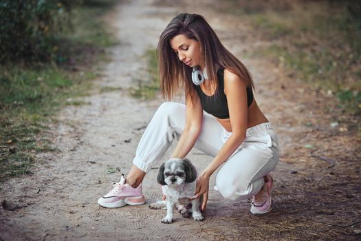 A young woman with her cute Shih Tzu is sitting on a path in the woods.