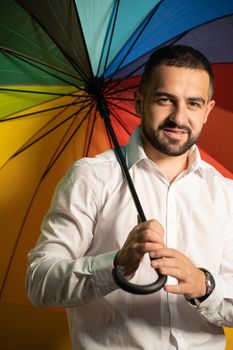 Straight handsome guy with a rainbow umbrella behind his back. Healthy fashion lifestyle, people sincere emotions, cold season concept. Handsome guy in support of LGBTQ society.