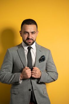 Holding jacket handsome slightly smiling young businessman wearing grey suit with one hand lifted standing half sideways isolated on yellow background. 