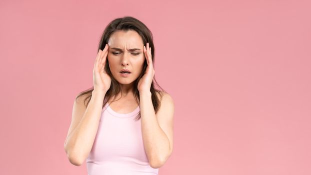 Have a migraine or severe headache while massaging the temporal lobe of the head young woman wearing pink t-shirt holding hands on head. Human emotions, facial expression concept.