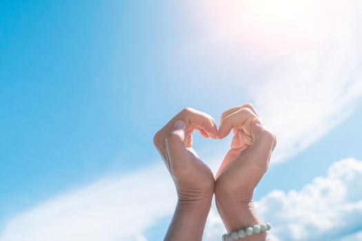 Woman hand do heart shape on blue sky and beach background.