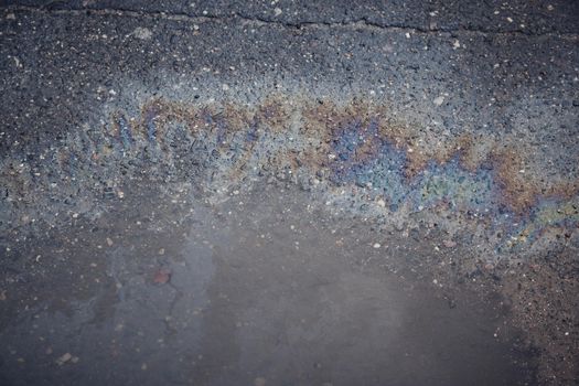 Gas stain on wet asphalt caused by a leak under a car or truck, abstract background