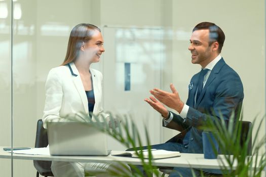 Smiling diverse business partners young man and woman discussing project sitting in a modern bright meeting. Handsome young businessman and a woman cooperating working in the office. 