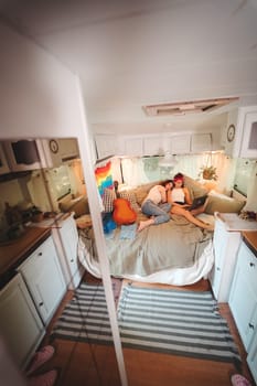 Portrait of a cute lesbian couple. Two girls spend time tenderly together watching movie on laptop in a camper trailer with LGBT flag on the wall. Love and attitude. LGBT concept. High quality photo