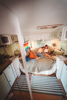 Portrait of a cute lesbian couple. Two girls spend time tenderly together watching movie on laptop in a camper trailer with LGBT flag on the wall. Love and attitude. LGBT concept. High quality photo