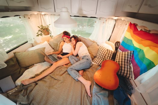 Portrait of a cute lesbian couple. Two girls spend time tenderly together watching movie on laptop in a camper trailer with LGBT flag on the wall. Love and attitude. LGBT concept. High quality photo