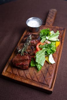 juicy beef steak with herbs and sauce on a wooden board.