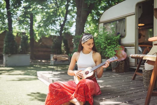 Happy hippie girl are having a good time with playing on guitar in camper trailer. Holiday, vacation, trip concept.High quality photo