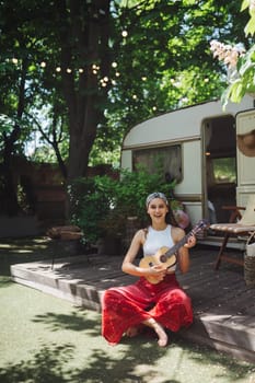 Happy hippie girl are having a good time with playing on guitar in camper trailer. Holiday, vacation, trip concept.High quality photo