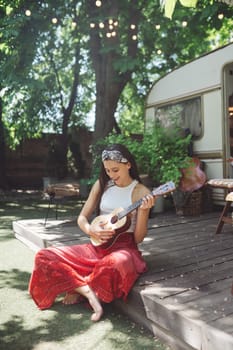 Happy hippie girl are having a good time with playing on guitar in camper trailer. Holiday, vacation, trip concept.High quality photo