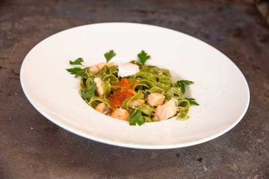 green pasta with salmon and red caviar and greens in a white plate.