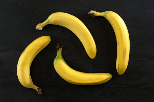 Flat lay photo - 4 bananas on black desk.