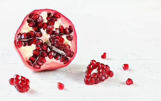 Half of pomegranate with some small gem like fruits scattered on white board. Space for text in upper right corner