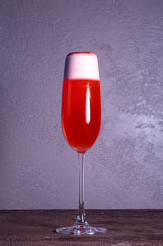 red refreshing cocktail with foam in a glass on a gray background.