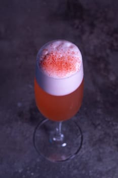 top view of a red refreshing cocktail with foam in a glass on a gray background.