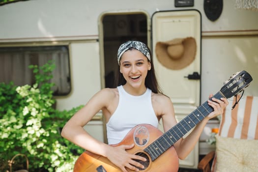 Happy hippie girl are having a good time with playing on guitar in camper trailer. Holiday, vacation, trip concept.High quality photo