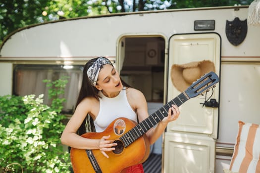 Happy hippie girl are having a good time with playing on guitar in camper trailer. Holiday, vacation, trip concept.High quality photo