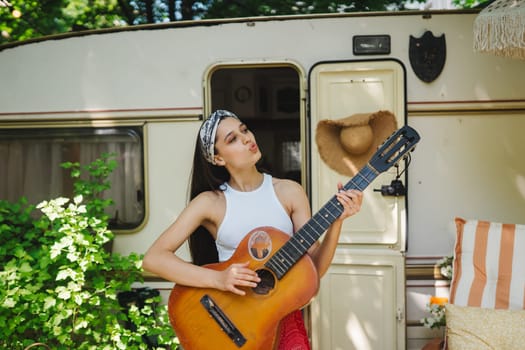 Happy hippie girl are having a good time with playing on guitar in camper trailer. Holiday, vacation, trip concept.High quality photo