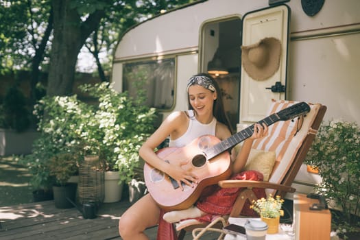 Happy hippie girl are having a good time with playing on guitar in camper trailer. Holiday, vacation, trip concept.High quality photo
