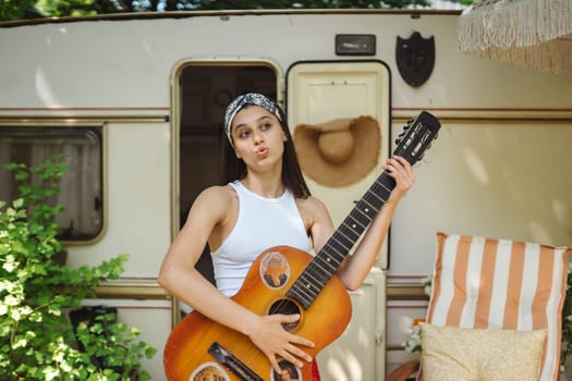Happy hippie girl are having a good time with playing on guitar in camper trailer. Holiday, vacation, trip concept.High quality photo