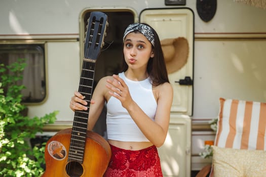 Happy hippie girl are having a good time with playing on guitar in camper trailer. Holiday, vacation, trip concept.High quality photo