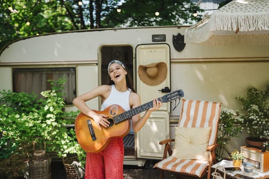 Happy hippie girl are having a good time with playing on guitar in camper trailer. Holiday, vacation, trip concept.High quality photo