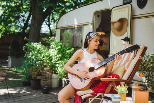 Happy hippie girl are having a good time with playing on guitar in camper trailer. Holiday, vacation, trip concept.High quality photo