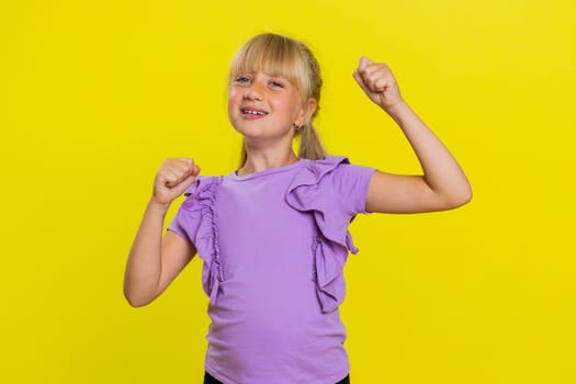 Young preteen child girl kid shouting, raising fists in gesture I did it, celebrating success, winning, birthday, lottery jackpot goal achievemen. Little cute children isolated on yellow background