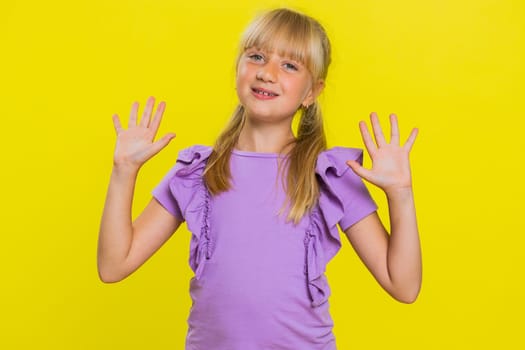 Young cute blonde school girl smiling friendly at camera and waving hands gesturing hello or goodbye, welcoming with hospitable expression. Preteen female child kid isolated on yellow background