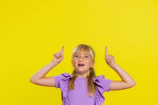 Happy cute girl showing thumbs up pointing empty place up, advertising area for commercial text, copy space for goods promotion banner, copy-space. Young child kid. Studio shot on yellow background