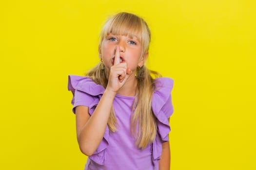 Shh be quiet please. Preteen child girl kid presses index finger to lips makes silence hush gesture sign do not tells gossip secret. Little cute children isolated alone on studio yellow background