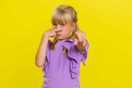 I am watching you. Young cute blonde school girl pointing at her eyes and camera, show I am watching you gesture, spying on someone. Preteen female child kid isolated on studio yellow background