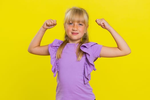 I am strong and healthy. Young cute girl showing biceps and looking confident feeling power strength to fight for rights, energy to gain success win. Preteen blonde child kid on yellow background