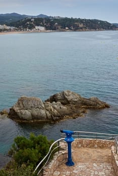 Sea view rocks and tourist telescope. Sea Rocks Telescope Lookout. Stationary binoculars, telescope, tower viewer or scope, ocean waves on rocky craggy beach. Magnifier or spyglass row. Coin Operated Binocular viewer next to the waterside promenade.