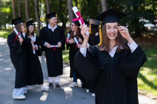 Group of happy students in graduation gowns outdoors. A young girl boasts of her diploma