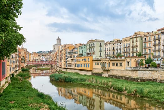 Colorful yellow and orange houses and bridge Pont de Sant Agusti reflected in water river Onyar, in Girona, Catalonia, Spain. Church of Sant Feliu and Saint Mary Cathedral at background. BRIDGE in the old town Girona, Catalonia, Spain, Europe, girones, girona, old town, view of the colorful house facades of the jewish quarter on the onyar river