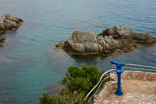 Sea view rocks and tourist telescope. Sea Rocks Telescope Lookout. Stationary binoculars, telescope, tower viewer or scope, ocean waves on rocky craggy beach. Magnifier or spyglass row. Coin Operated Binocular viewer next to the waterside promenade.