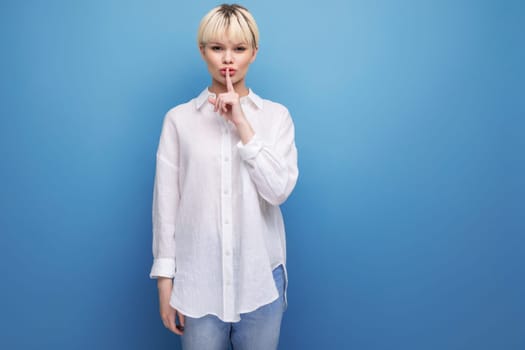 young calm pretty blonde businesswoman in a white shirt keeps a secret on the background with copy space. people lifestyle concept.