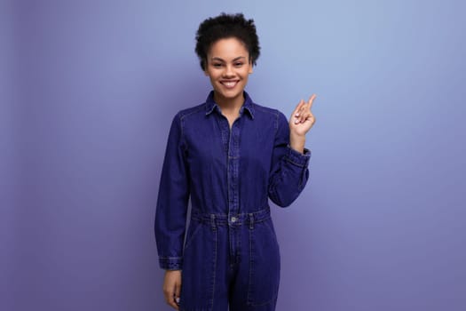 smart slim young hispanic brunette woman with fluffy curly hair in a blue denim suit is actively gesturing with her hands.