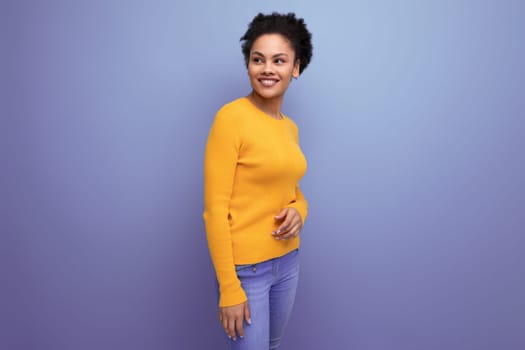 pretty confident 20s latin woman with afro hair in casual yellow sweater on studio background with copy space.