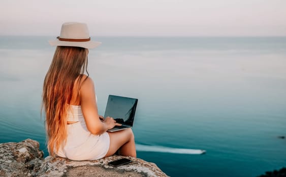 Digital nomad, Business woman working on laptop by the sea. Pretty lady typing on computer by the sea at sunset, makes a business transaction online from a distance. Freelance, remote work on vacation